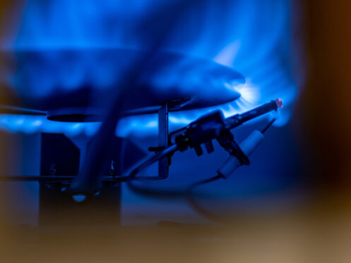 A close-up view of a lit blue gas flame on a stovetop burner, with an igniter and wires visible in the foreground, highlights the pilot light importance for safely igniting and maintaining the burner flame. | High 5 Plumbing, Heating & Cooling