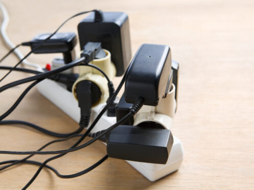A power strip on a wooden surface with several plugs, adapters, and chargers connected, creating a clutter of cords and an overloaded extension socket, highlighting the importance of electrical cord safety. | High 5 Plumbing, Heating & Cooling
