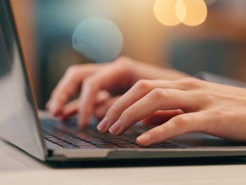 Close-up of a person’s hands typing on a laptop keyboard, with a blurred background featuring warm lighting. The scene suggests work or study—perhaps researching ways to save water or cut the water bill at home. | High 5 Plumbing, Heating & Cooling