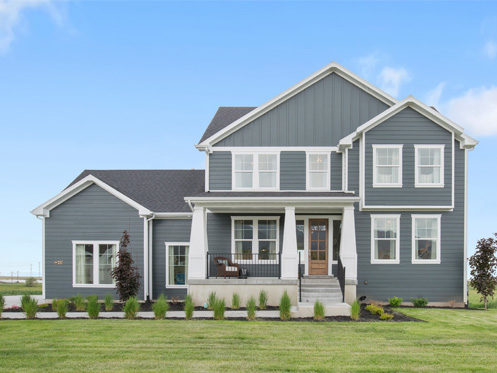 A two-story modern house with gray siding, white trim, and a covered front porch. The yard is landscaped with grass, shrubs, and small trees. The sky is clear with a few clouds. | High 5 Plumbing, Heating & Cooling