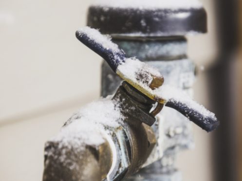 A close-up of an outdoor water faucet covered in snow and ice, highlighting cold winter weather and the risk of frozen pipes. The metallic faucet with a blue handle serves as a reminder of what to do when pipes freeze. | High 5 Plumbing, Heating & Cooling