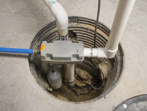 A sump pump system installed in a basement pit includes PVC pipes for discharge, a float switch, electrical wiring, and a corrugated liner set into concrete—ideal for effective water removal and easy regular sump pump maintenance. | High 5 Plumbing, Heating & Cooling
