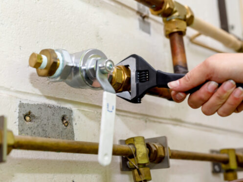 A hand holding a wrench, ready to install a vacuum breaker on an outdoor faucet. | High 5 Plumbing, Heating & Cooling